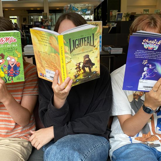 Tre børn sidder i en sofa og læser