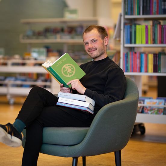 Mand der sidder i en lænestol med en bog om græske mytologier i hånden