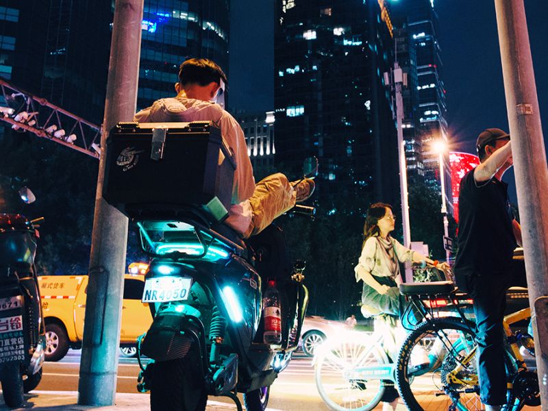 Nattebillede fra kinesisk storby. Folk på scooter og cykler.